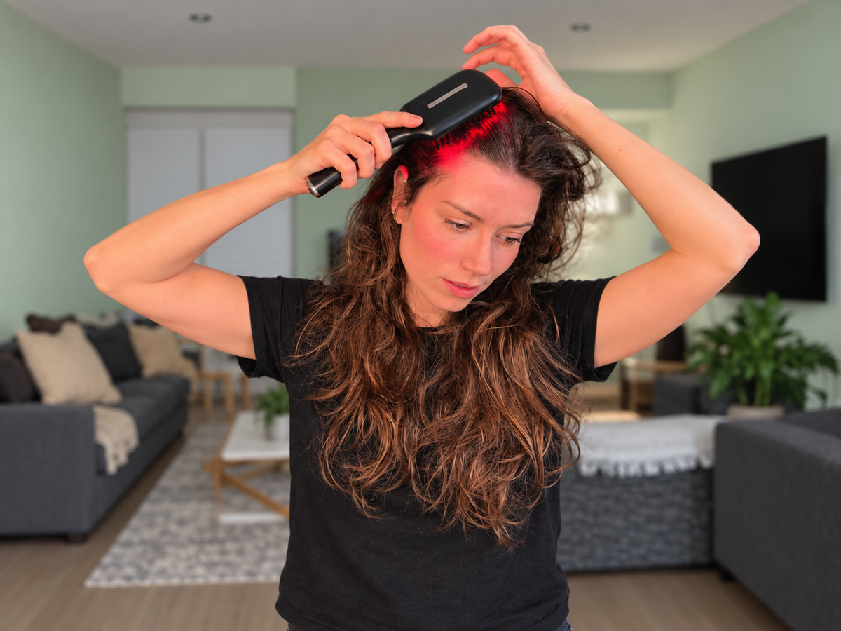 Woman using the black Soodox hair oil dispensing brush with red light in a sage green living room